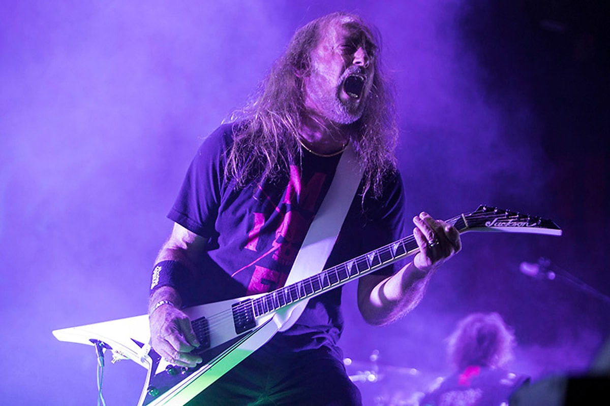 A guitarist performs in purple stage light.