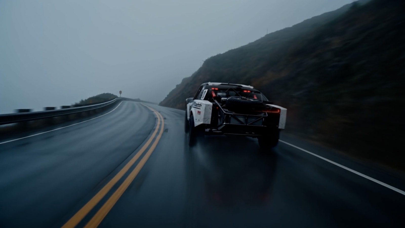 Rear view of a car with exposed bodywork on a wet mountain road.