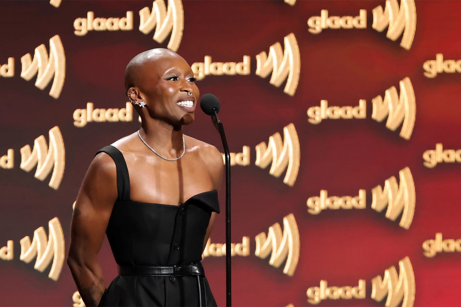 A speaker at a microphone against a repeating gold GLAAD logo backdrop.