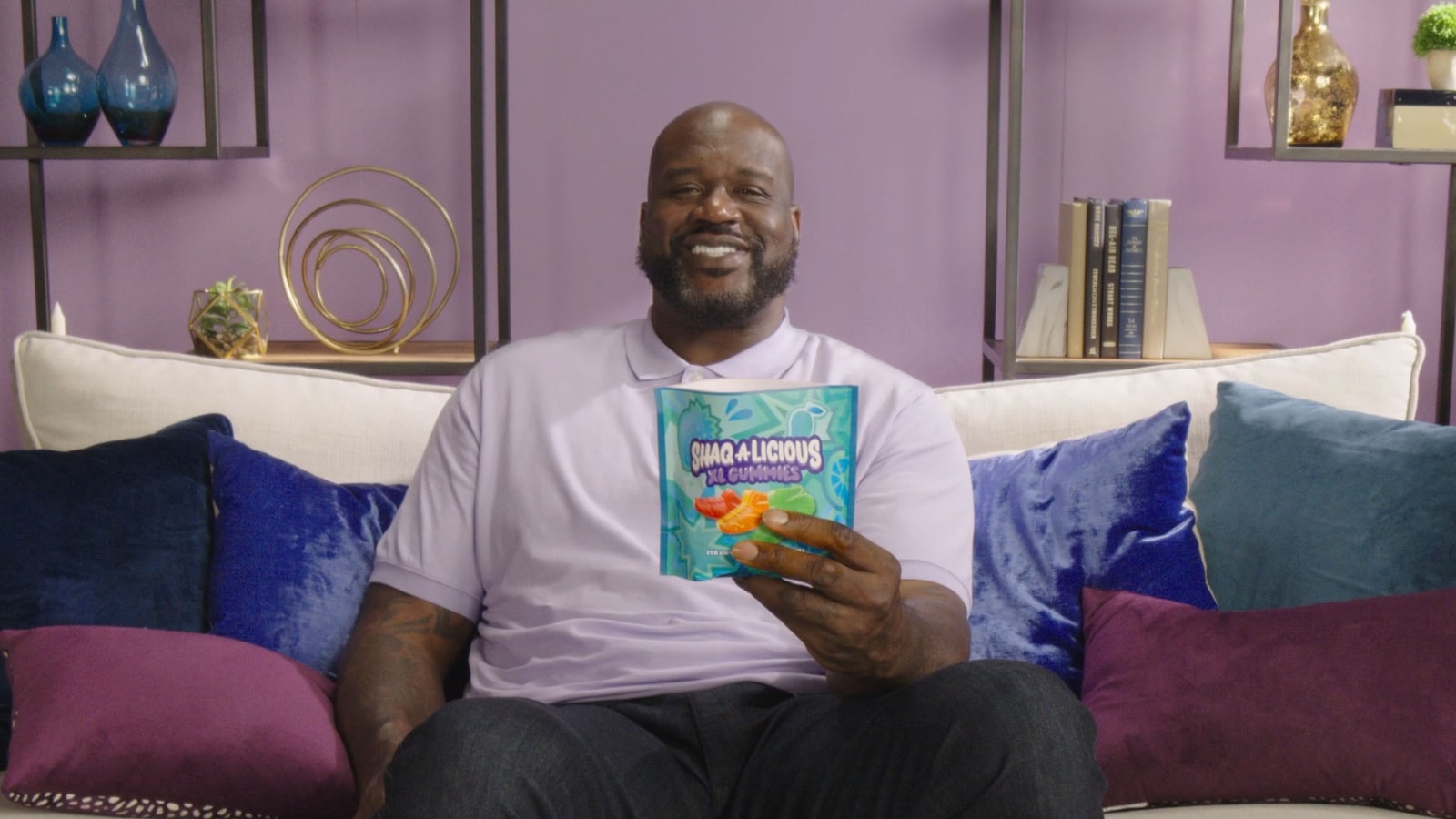 Shaquille O’Neal holds a bag of Shaqalicious gummies on a couch.