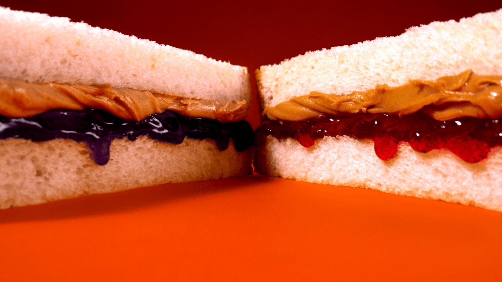 Peanut butter and jelly sandwich halves on an orange background.