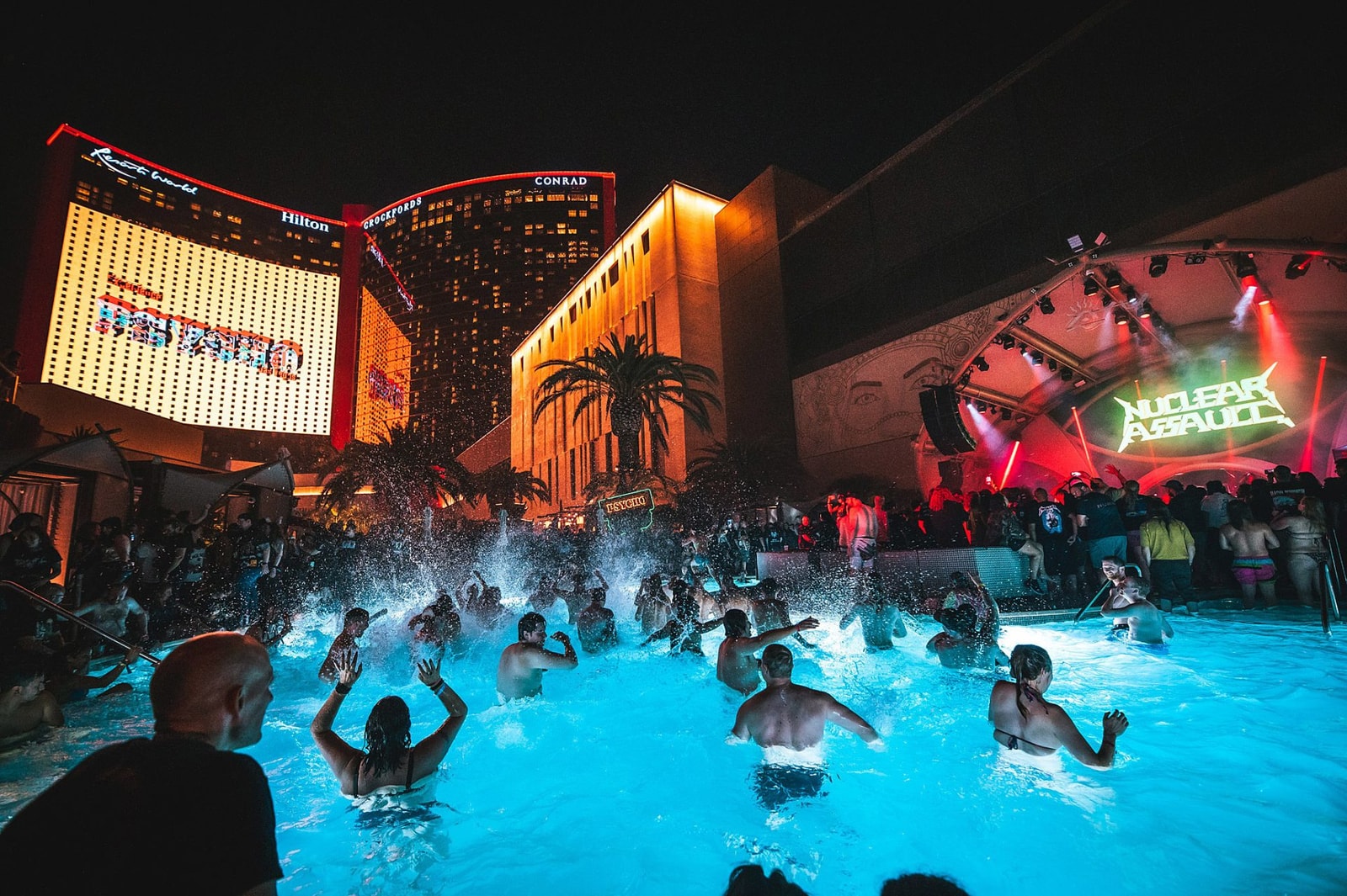 Festivalgoers gather in a pool in front of an illuminated stage.