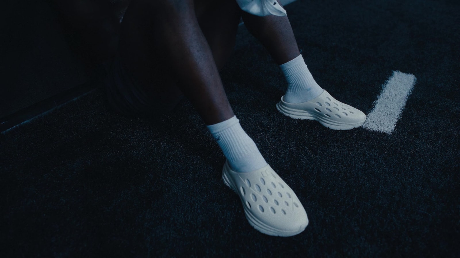 Close-up of white KANE shoes worn with white socks on a dark gym floor.