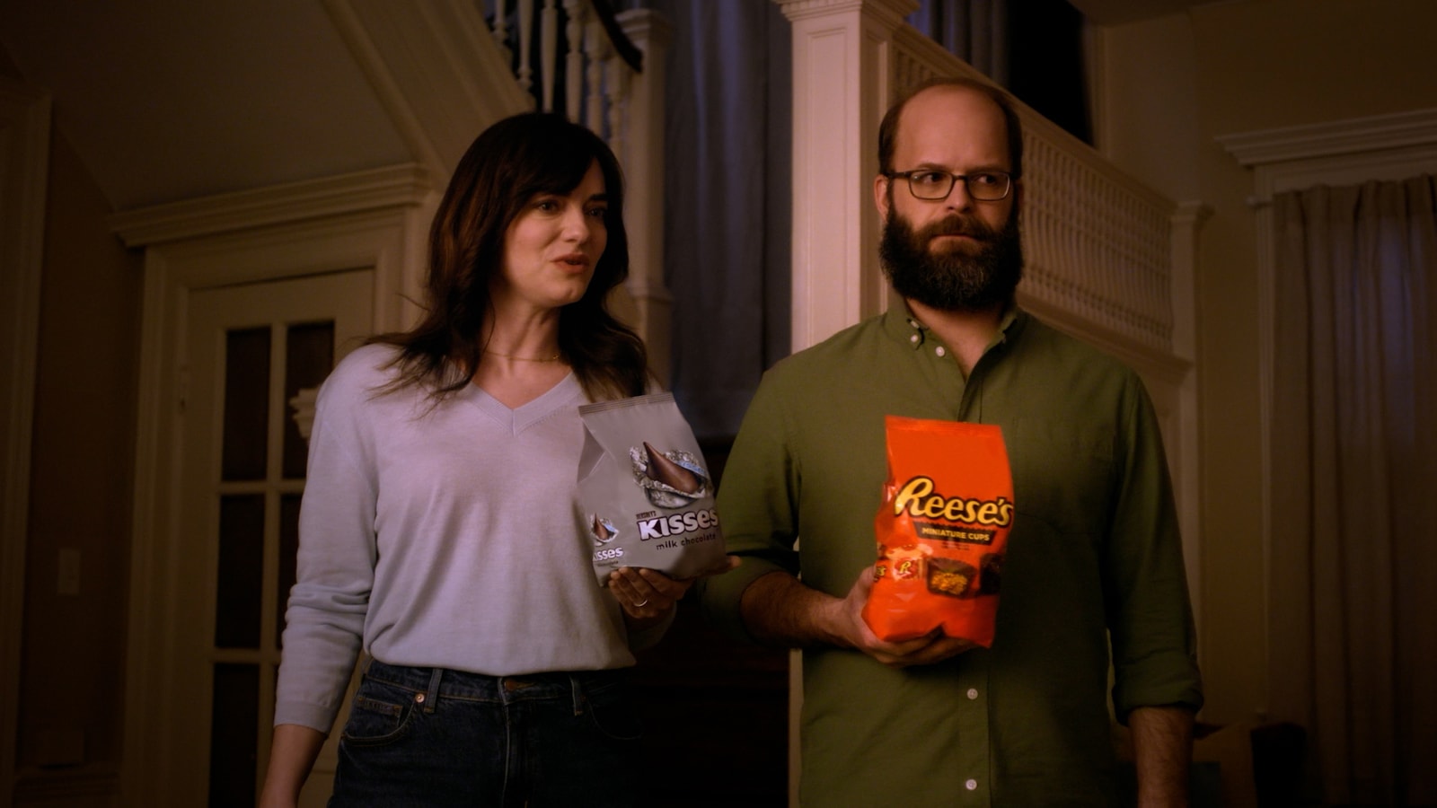 Two adults hold Hershey’s Kisses and Reese’s bags in a doorway.