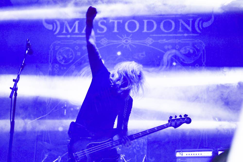A silhouetted performer stands before a purple Mastodon stage backdrop.