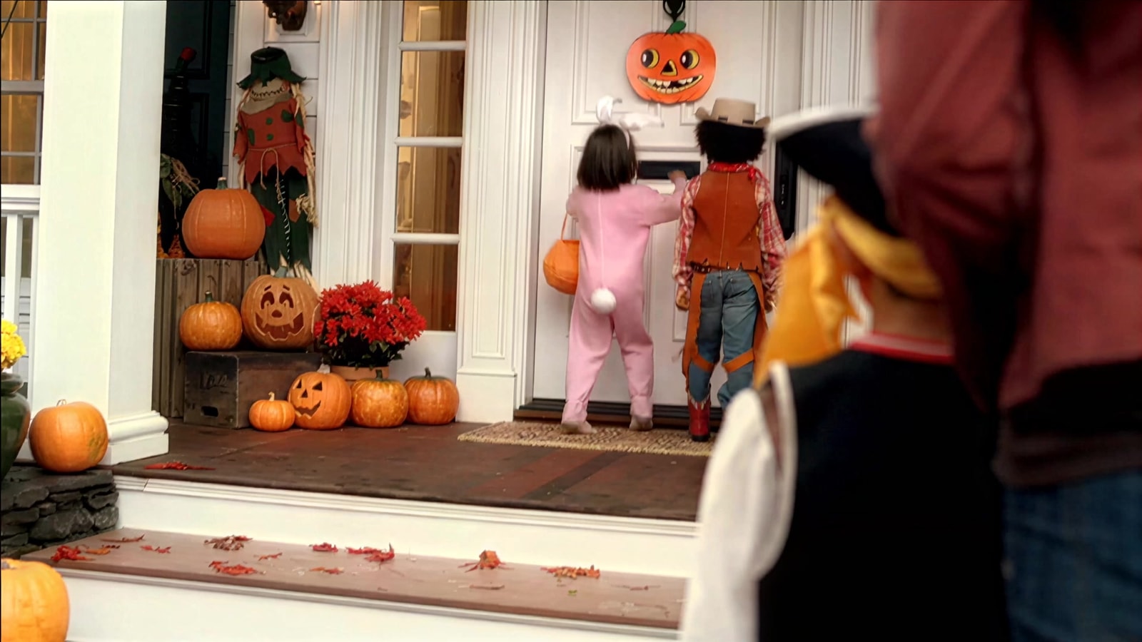 Costumed trick-or-treaters gather at a pumpkin-decorated front door.