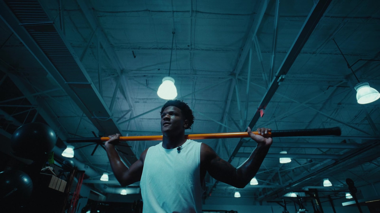 Derrek Cooper trains with a bar across his shoulders beneath the blue-lit gym ceiling.