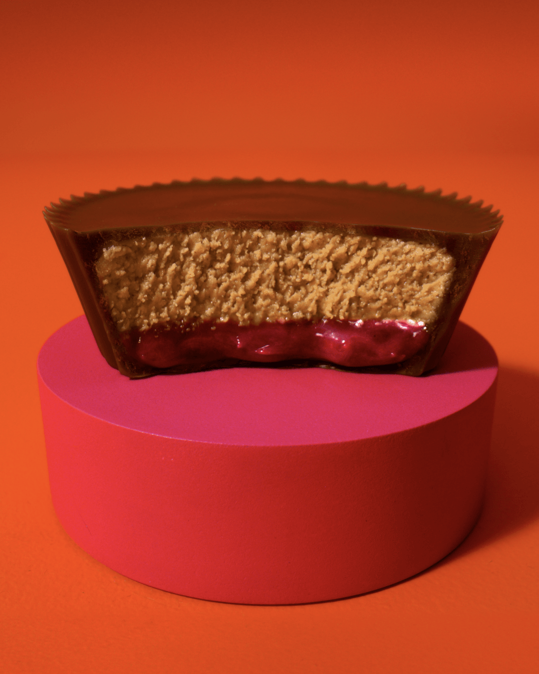 A strawberry-filled Reese’s PB&J cup sits on a pink pedestal.